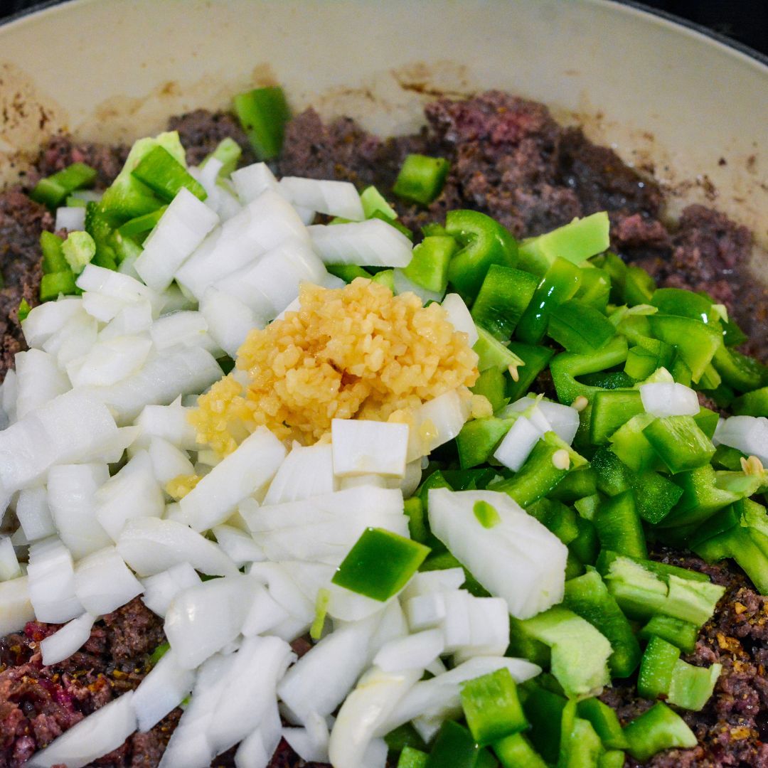 Add the diced onion and green pepper to the skillet with the browned ground beef. Top off with the minced garlic. Cook until the vegetables are soft and fragrant, about 4-5 minutes.