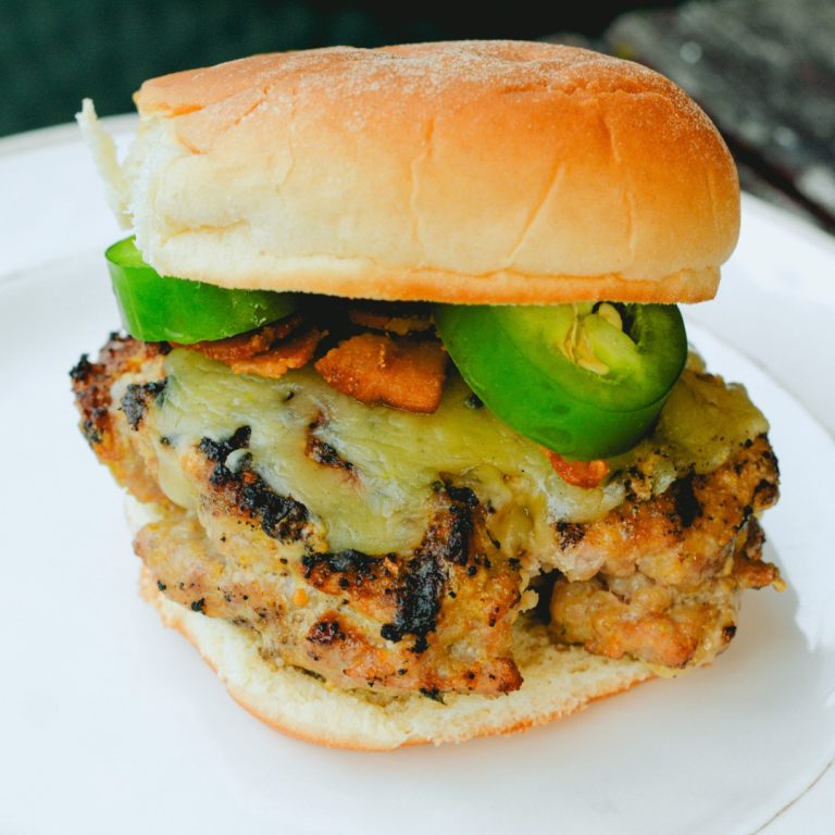 These jalapeno popper stuffed pork burgers are made with ground pork and filled with cream cheese, fresh jalapeno slices, and bacon pieces then topped with even more cheese for the perfect spicy pork burgers recipe.