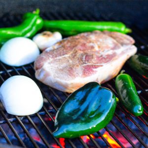 While the pork is smoking, you'll roast poblano and Anaheim peppers, jalapeños, onions, and garlic on the grill to create a zesty green chile sauce.