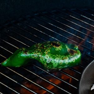 Begin by roasting the poblanos on the smoker to cause the peppers to blister for 10-15 minutes. Remove from the grill and put in a covered bowl for 10 minutes to allow to continue to cook. Then cut them in half and remove the seeds before chopping.