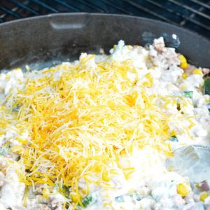 Add half the shredded cheese to the corn dip. Stir to mix together. Let's continue to smoke the corn dip for 30 minutes to an hour. The longer it cooks, the smokier the flavors will get.