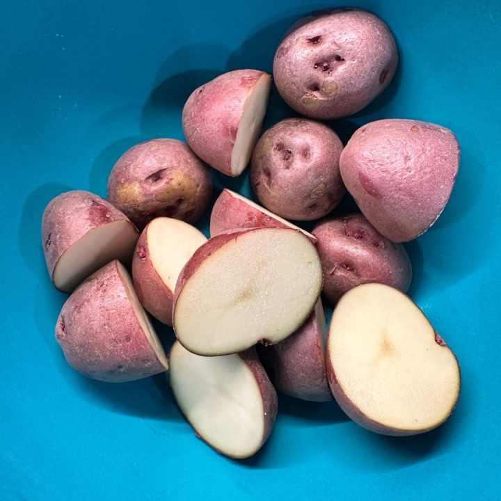 Wash and dry the potatoes thoroughly. Cut them in half to create a flat surface for maximum contact with the Parmesan crust.