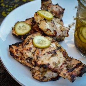 Pickle brined grilled chicken is made by marinating boneless, skinless chicken thighs in pickle juice, pickles, onions, garlic, peppercorns, and olive oil resulting in the juiciest grilled chicken.