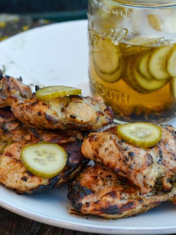 Pickle brined grilled chicken is made by marinating boneless, skinless chicken thighs in pickle juice, pickles, onions, garlic, peppercorns, and olive oil resulting in the juiciest grilled chicken.