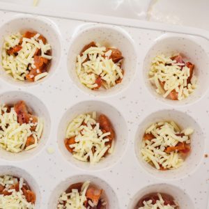 Add crumbled bacon pieces and shredded cheese to each muffin cup.