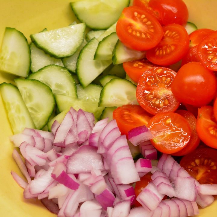 Start by preparing the vegetables. Dice the tomatoes and cucumber into bite-sized pieces and thinly slice the red onion. Once the vegetables are prepped, combine the diced tomatoes, cucumber, and sliced red onion in a large salad bowl.