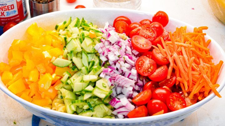 Dice and chop up the vegetables. Then, add the red onion, carrots, celery, bell peppers, peas, and shredded cheddar cheese to the cooked macaroni or pasta in a large bowl.