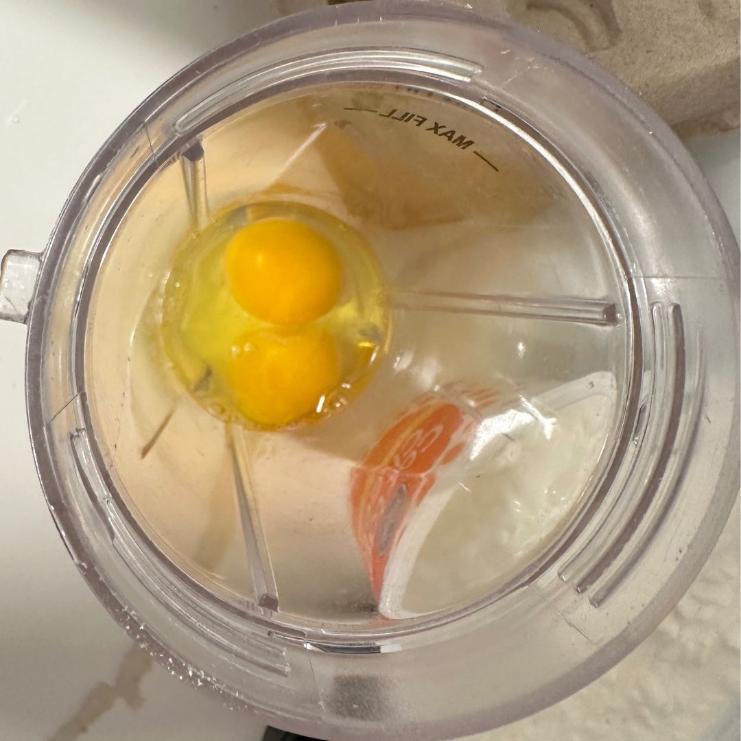 To make these quick and easy high-protein microwave egg bites, start by cracking two eggs into a a blender cup.