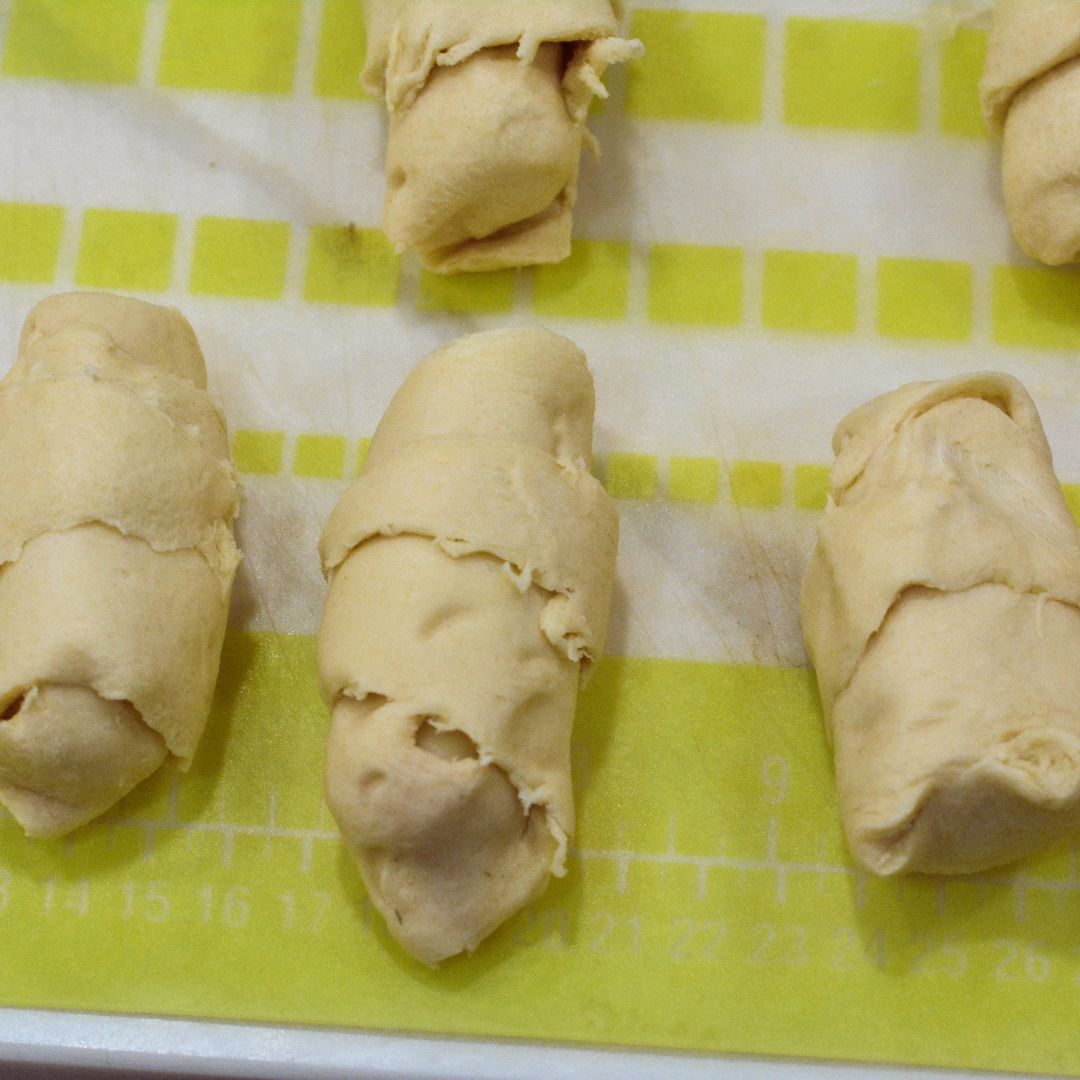 Roll the dough around the cheese stick, starting from the wide end and rolling towards the pointed end. Pinch any seams closed to prevent cheese from leaking out.