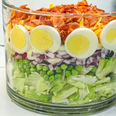 This easy 7-layer salad recipe is a crowd-pleaser with crisp romaine, peas, onions, bacon, eggs, cheese, and creamy dressing. Perfect for potlucks or make-ahead meals!