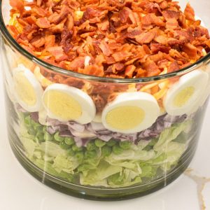 This easy 7-layer salad recipe is a crowd-pleaser with crisp romaine, peas, onions, bacon, eggs, cheese, and creamy dressing. Perfect for potlucks or make-ahead meals!