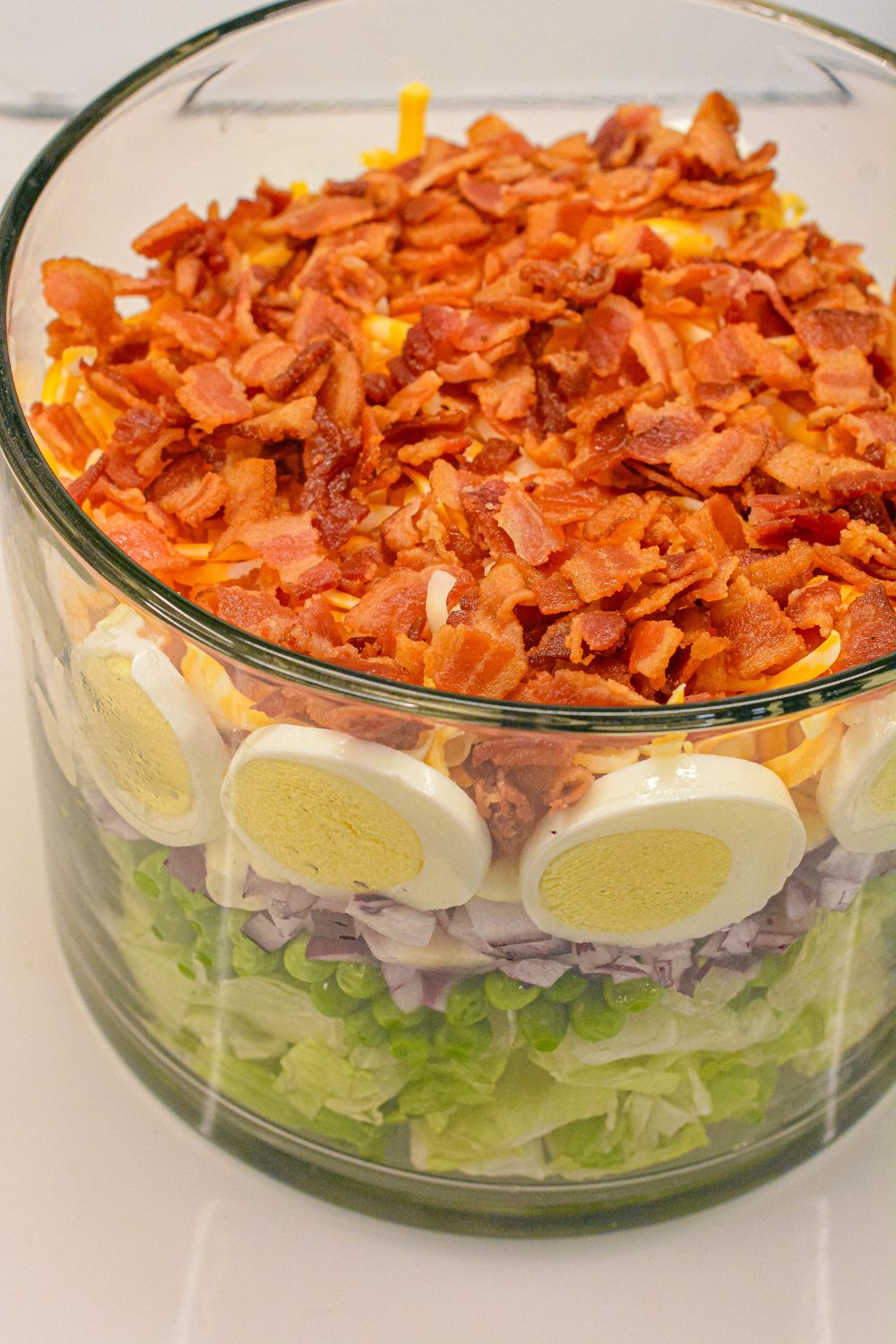 This easy 7-layer salad recipe is a crowd-pleaser with crisp romaine, peas, onions, bacon, eggs, cheese, and creamy dressing. Perfect for potlucks or make-ahead meals!